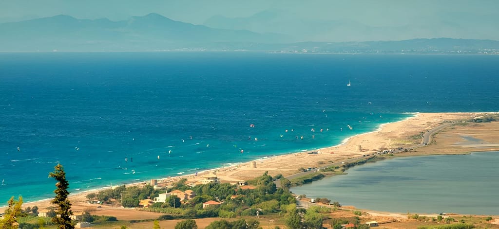 Kitesurf sulla spiaggia di Agios Ioannis a Lefkada, fotografata dalla strada panoramica per Tsoukalades, con il mare scintillante e il cielo azzurro.