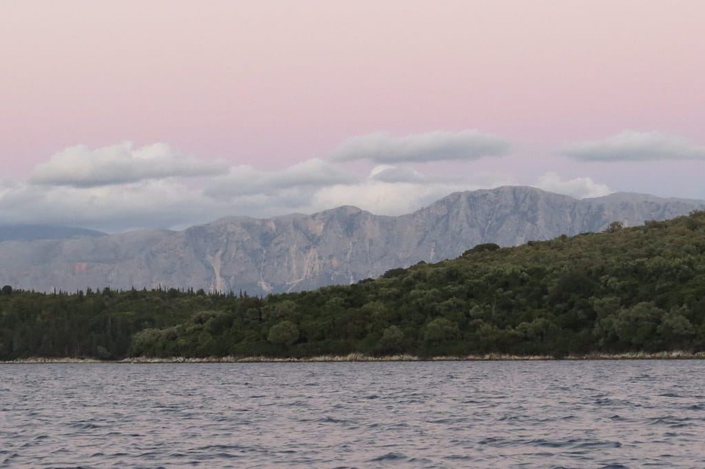 Il tramonto al largo di Nidri, con isole incorniciate da riflessi pastello che colorano il Mar Ionio.