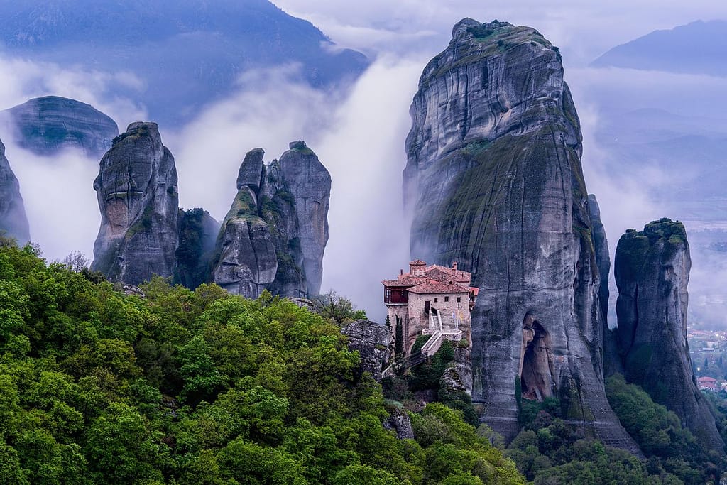 Le formazioni rocciose di Meteora immerse in una nebbia avvolgente che si alza in spirali suggestive.
