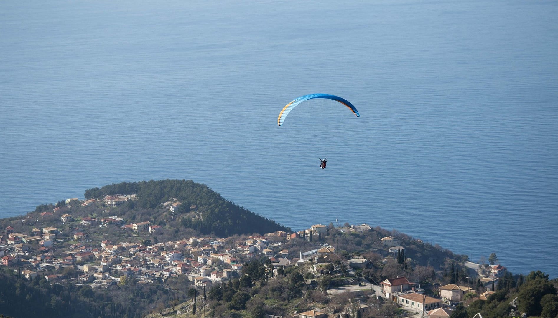 Un parapendio si libra con grazia sopra Kalamitsi, con il mare blu intenso che incornicia la scena e crea un panorama indimenticabile.