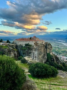 Un grande monastero ortodosso sorge maestoso sulla cima di una roccia scoscesa, dominando la pianura sottostante. Costruito secoli fa, il monastero si staglia contro un cielo drammatico, creando un'atmosfera cinematografica e suggestiva.