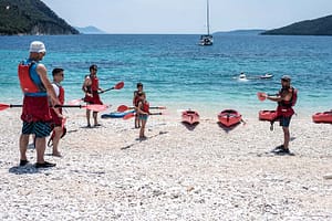 Kayaks sulla spiaggia di Poros, con adulti e bambini che ascoltano attentamente le istruzioni della guida prima di partire per il tour in kayak a Lefkada.