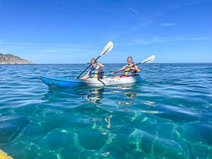 Una coppia sorridente mentre pagaia insieme in kayak nelle acque cristalline di Lefkada.