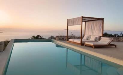 Piscina di Villa Rhea a Lefkada all’alba, con il mare illuminato da luce rosata, un letto a baldacchino e lettini prendisole che evocano relax e beatitudine.