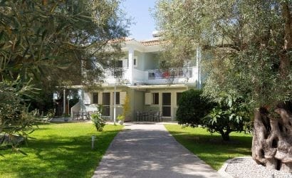 Vista degli esterni dell'edificio principale di Niki Apts, immerso in un ampio giardino curato con ulivi secolari, ad Agios Ioannis, Lefkada.