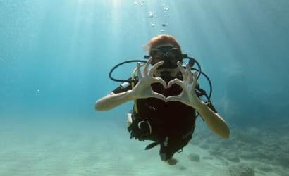 Principiante subacquea in acque cristalline a Lefkada, con le mani unite formando un cuore, simbolo di passione per il diving