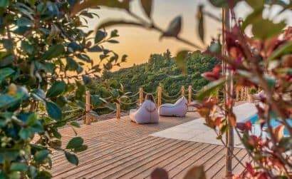 Terrazza panoramica di Eunoia Apts al tramonto, con due sedute accoglienti affacciate sulla piscina, circondate da fronde di gelso.