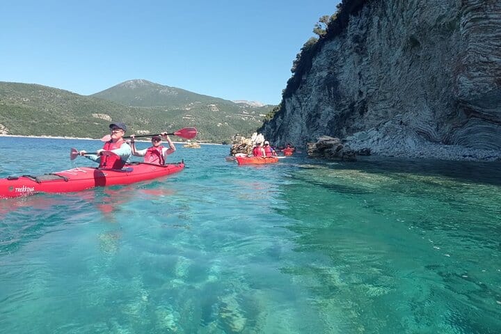 Un gruppo di partecipanti al tour in kayak pagaia lungo la costa di Meganissi, con il contrasto tra il fondo marino e le rocce che esalta la bellezza naturale.