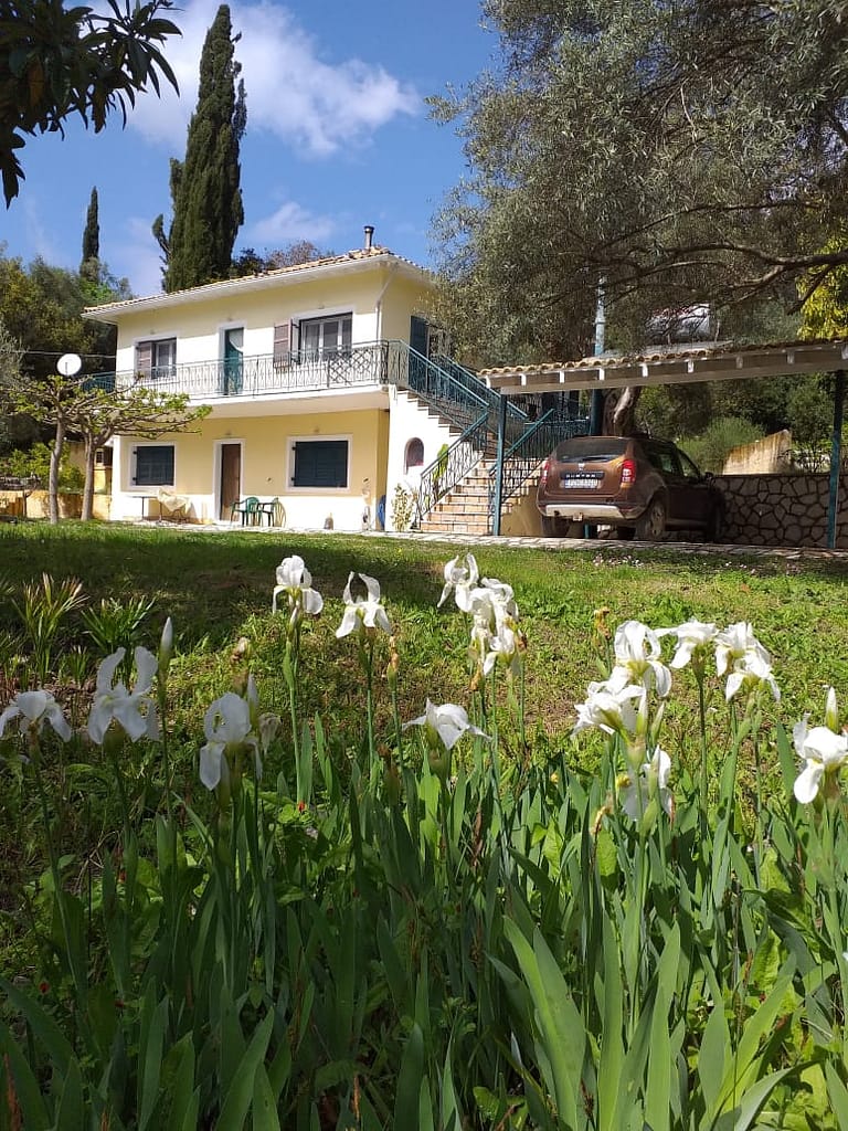 Casa Asteri a Geni, Lefkada, catturata durante la primavera. I gigli bianchi del giardino si stagliano contro il cielo azzurro, enfatizzando la grazia della villa immersa nella natura.