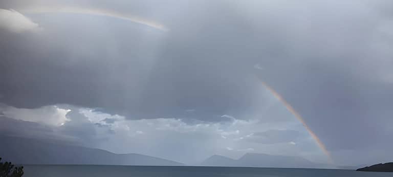 Un arcobaleno abbraccia l'isola di Kalamos, visibile dalla costa di Lefkada in una giornata nuvolosa.