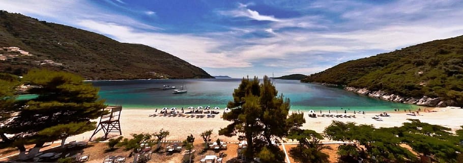 Vista panoramica della Baia di Rouda con la spiaggia di Mikros Gialos, caratterizzata da acque limpide che riflettono la vegetazione rigogliosa circostante.