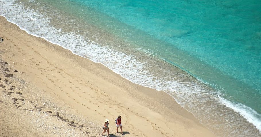 Coppia che cammina sulla spiaggia di Pefkoulia a Lefkada, ripresa dall'alto con il mare turchese sullo sfondo.