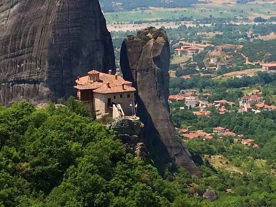 Un Monastero di Meteora sospeso sopra un picco roccioso, circondato da pareti di altri pinnacoli e con la città di Kalambaka visibile sullo sfondo.