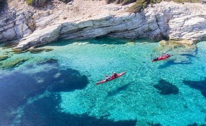 Vista dall'alto di due kayak in navigazione su un fondale sottocosta dai colori straordinari, con acque cristalline.