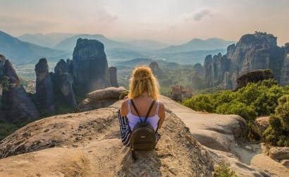 Una giovane donna seduta su una roccia, affascinata dalle spettacolari formazioni rocciose di Meteora.